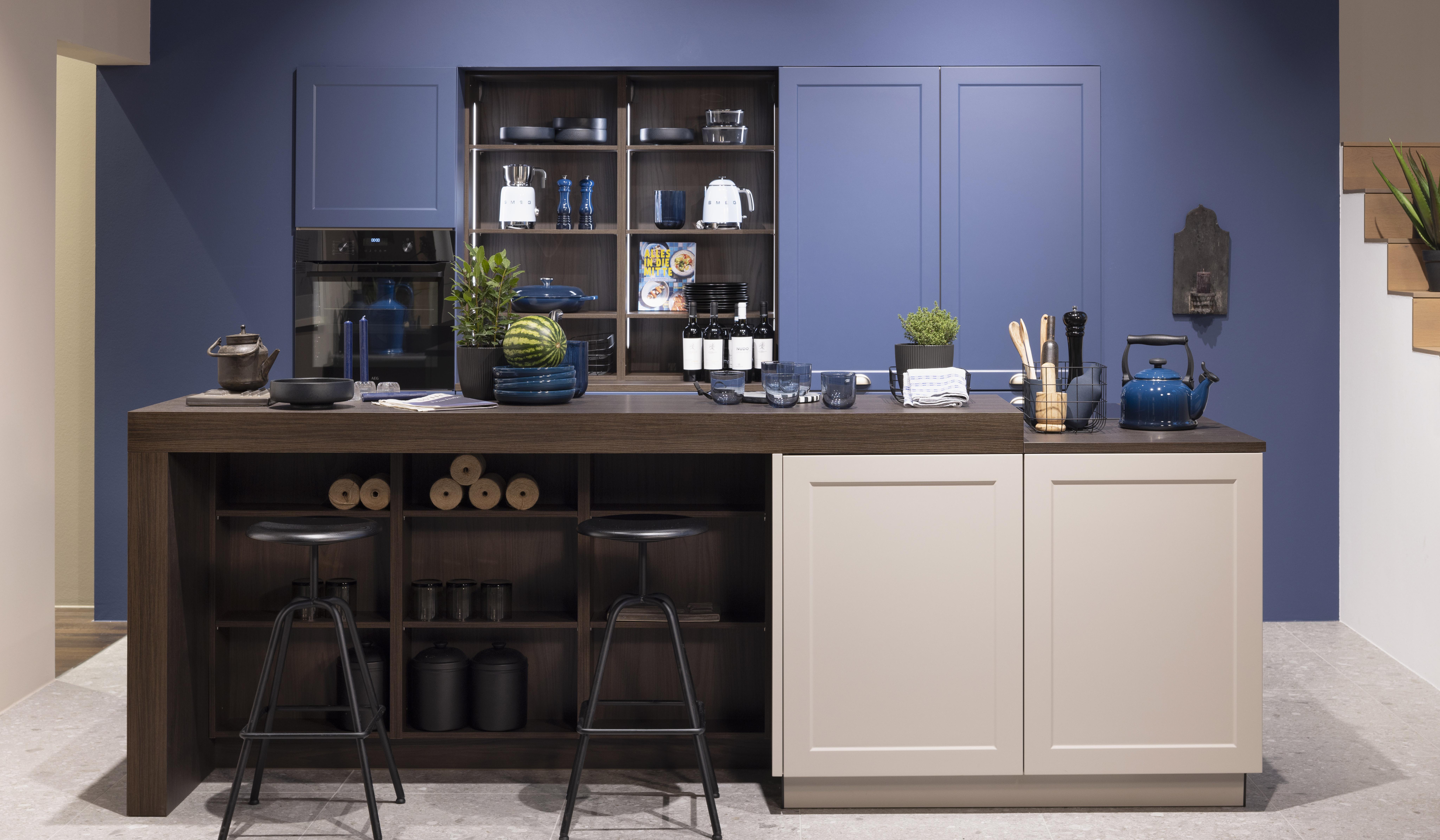 Moderne Küche mit Kochinsel, blauer Wand und Regalen, zwei schwarze Hocker davor.